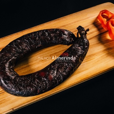 Chouriço escuro em formato circular numa tábua de madeira com pimento vermelho fatiado