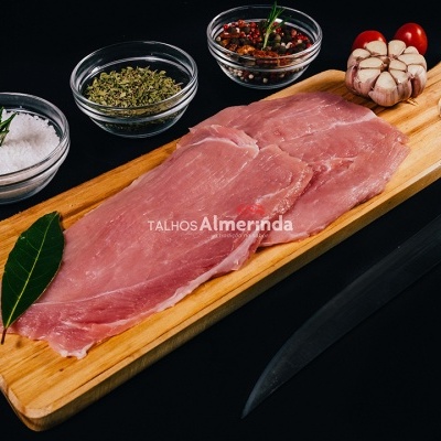 Bife cru rosa numa tábua de madeira com alho, tomatinhos, uma folha de louro e pequenos recipientes com sal, ervas e pimenta