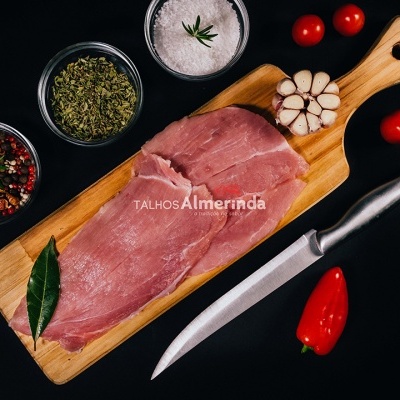 Carne crua sobre tábua de madeira com alho, tomate, pimento, faca e especiarias