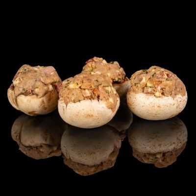 Quatro cogumelos recheados sobre superfície preta refletora