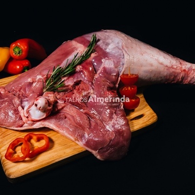 Pernil de carne crua numa tábua de madeira com pimentos e alecrim