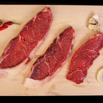 Três bifes crus com especiarias numa tábua de madeira