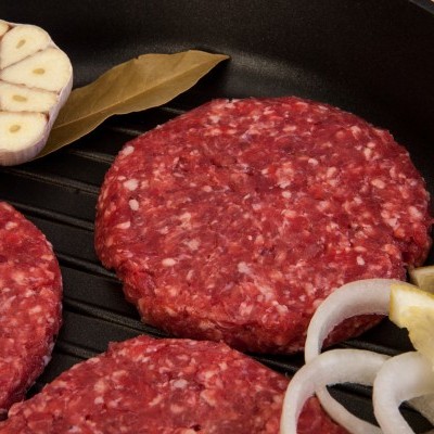 Hambúrgueres crus, alho, malagueta, folha de louro, cebola e limão numa frigideira.