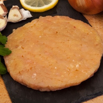 Hambúrguer de frango cru redondo em tábua preta com alho, limão, salsa, cebola e pimenta-do-reino