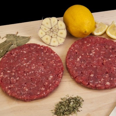 Hambúrgueres crus numa tábua com limão, alho, ervas, faca e garfo