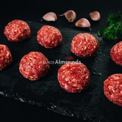 Oito almôndegas de carne crua numa tábua preta com dentes de alho e salsa