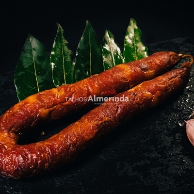 Chouriço curado com folhas verdes e dentes de alho sobre placa preta