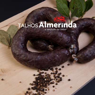 Enchidos escuros sobre tábua de madeira com folhas verdes e pimenta preta