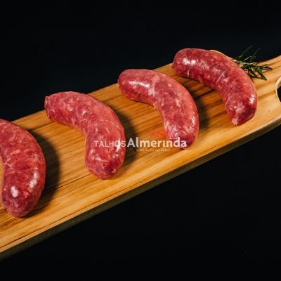 Quatro salsichas cruas numa tábua de madeira clara sobre fundo preto