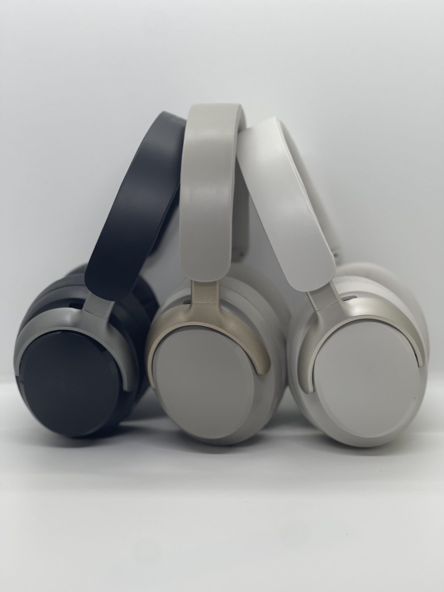 Headphones Heavy Bass 100 Três headphones sem fio em cores cinzento escuro, cinzento claro e branco sobre superfície branca