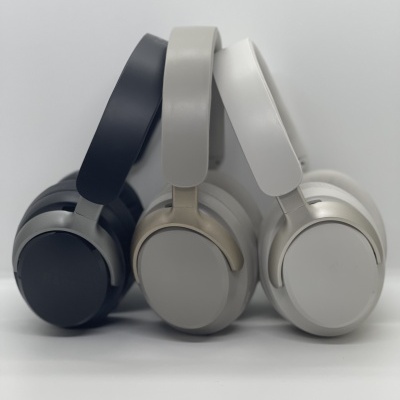 Três headphones sem fio em cores cinzento escuro, cinzento claro e branco sobre superfície branca
