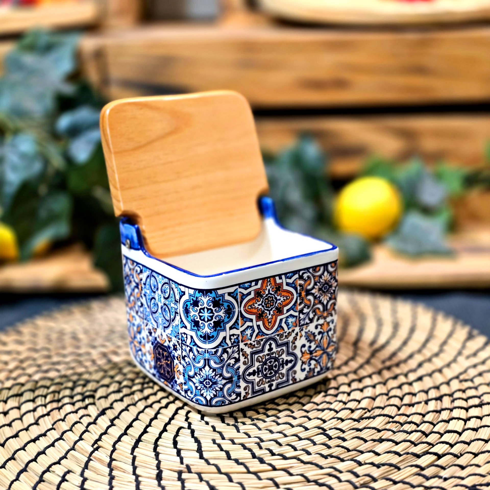 Saleiro c/ Tampa de Madeira Recipiente quadrado de cerâmica colorida com tampa de madeira sobre tapete redondo de fibras naturais.