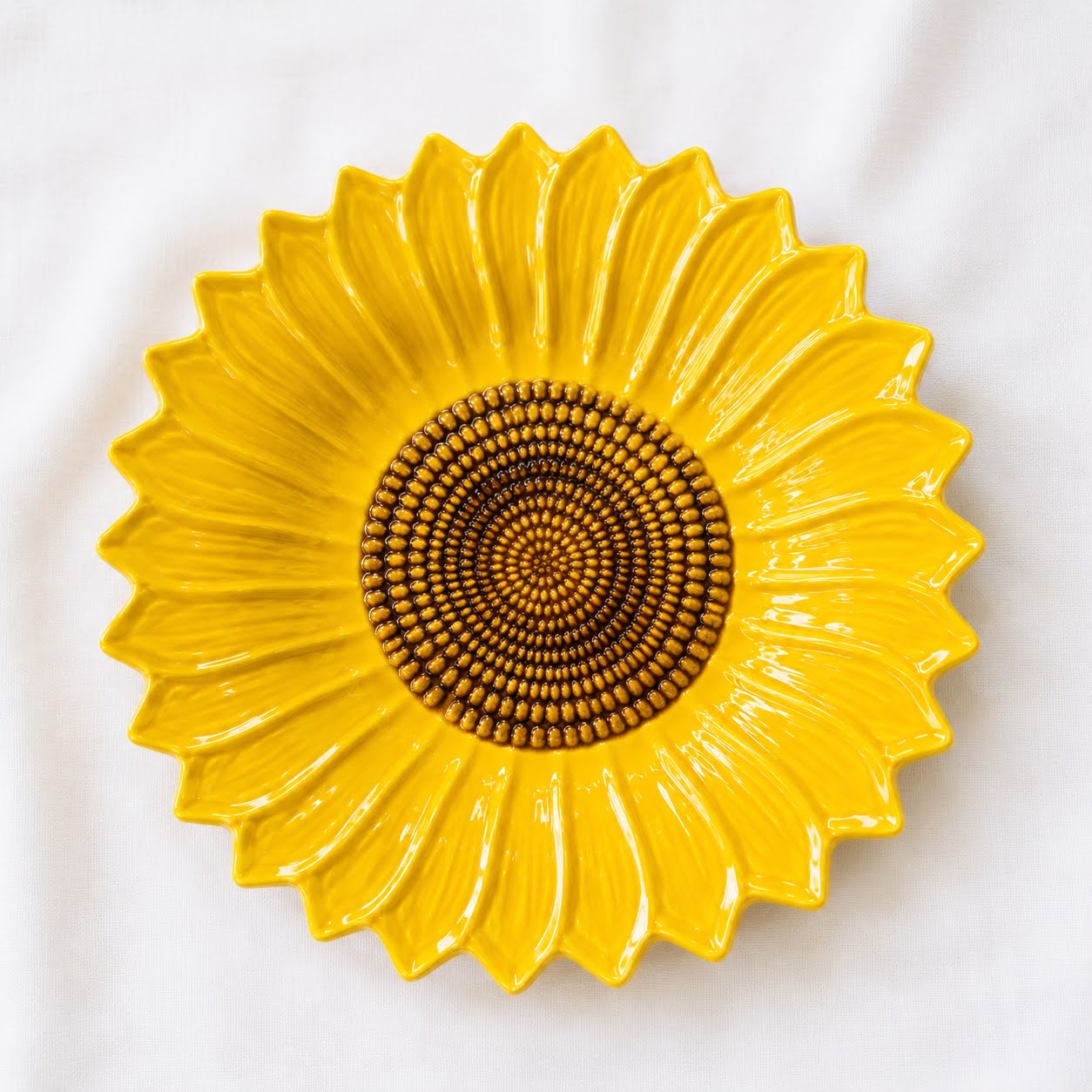 Coleção Girassóis Prato cerâmico amarelo em forma de girassol sobre tecido branco