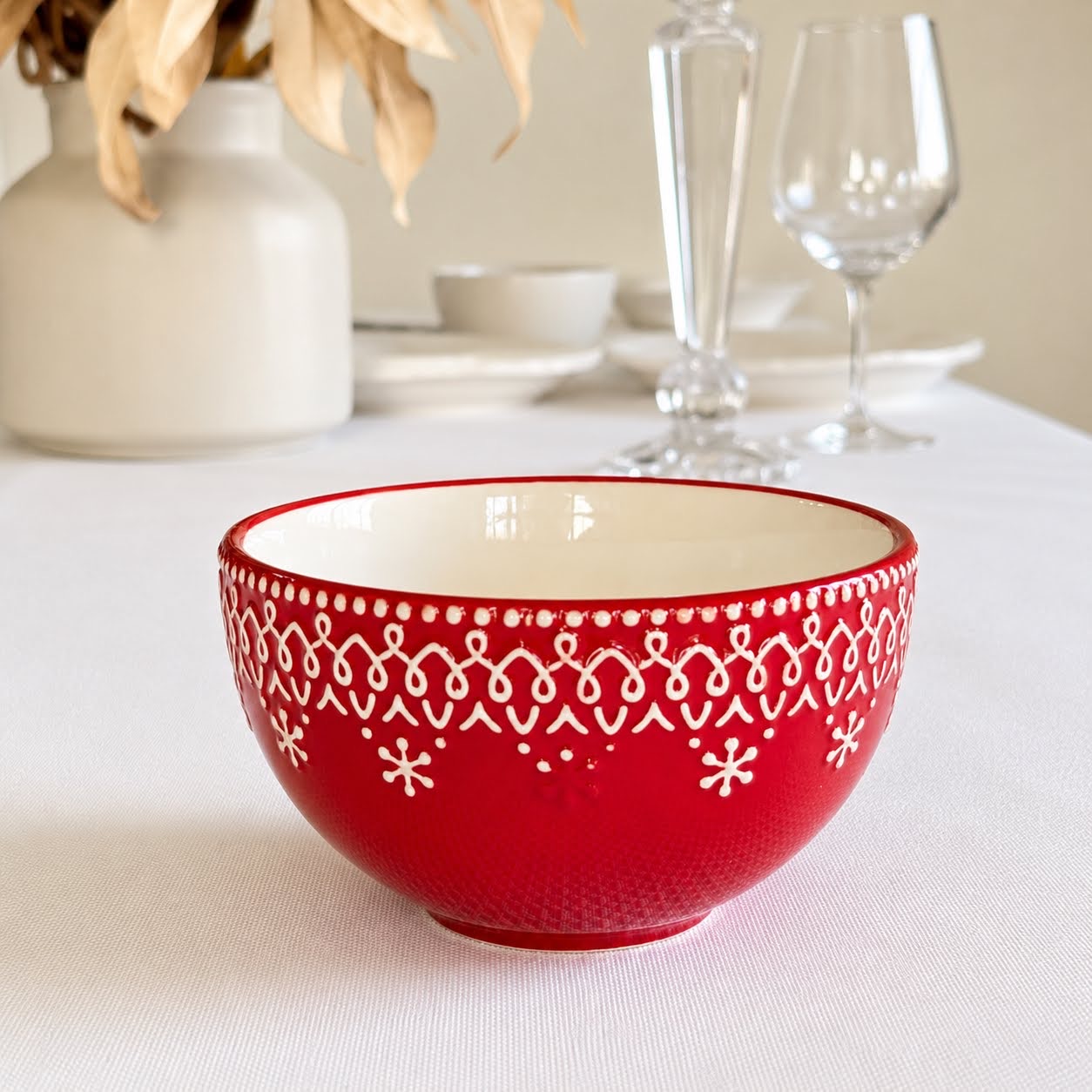 Coleção Grés Decorado Vermelho Taça de cerâmica vermelha com padrão branco em relevo sobre mesa com toalha branca.