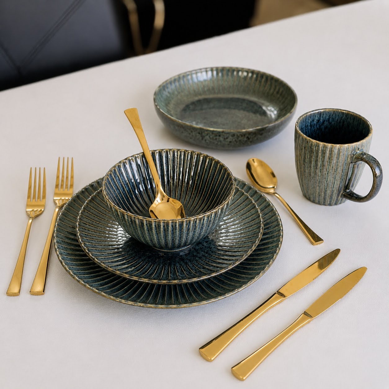 Conjunto de Louça de Mesa Azul Petróleo com Relevo Conjunto de loiça cerâmica azul com talheres dourados sobre mesa branca