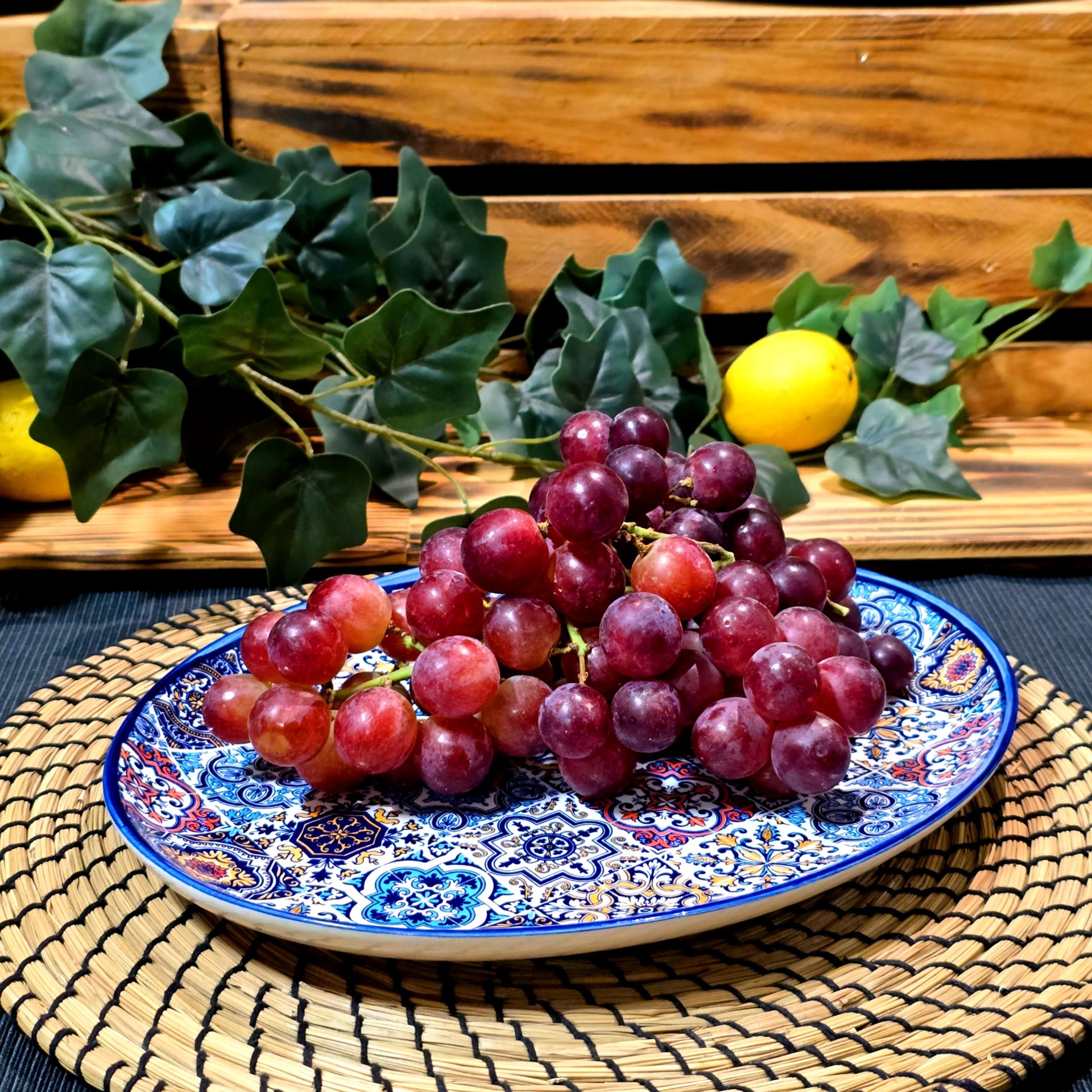 Travessinha e Travessa Oval XL Cacho de uvas roxas num prato cerâmico decorado com folhas verdes e limão ao fundo