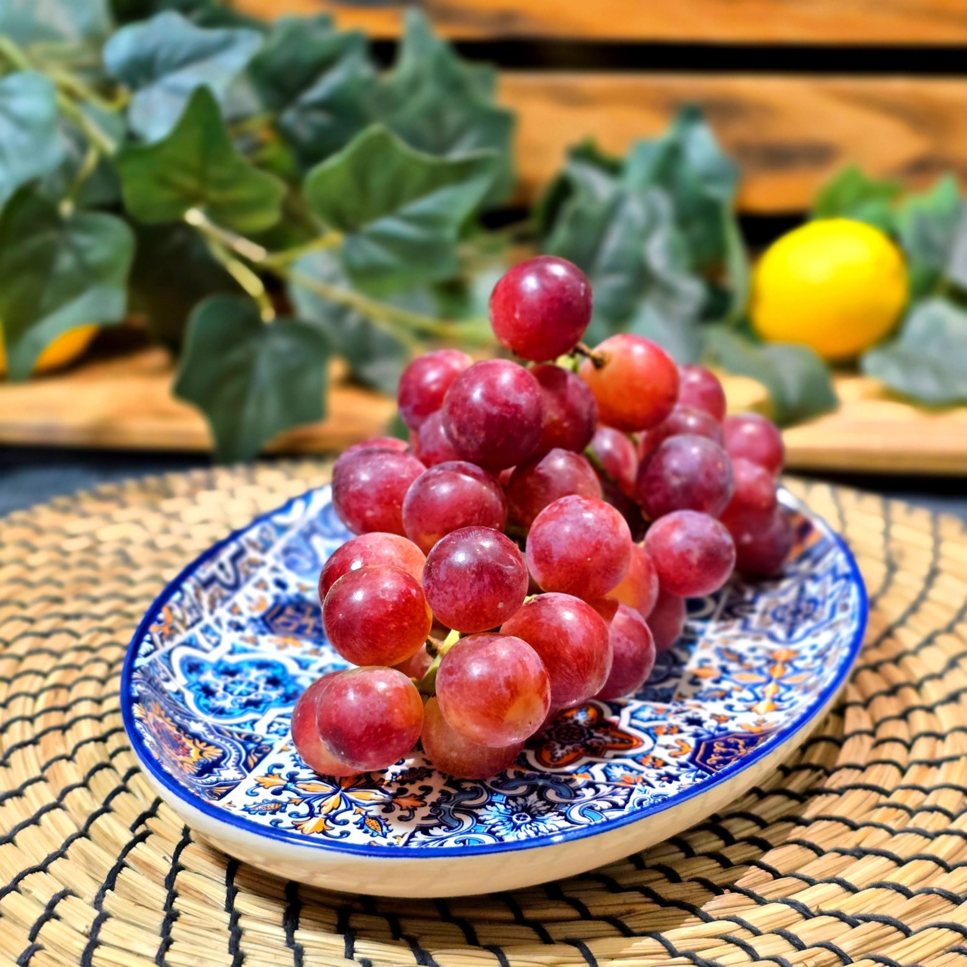 Travessinha e Travessa Oval XL Cacho de uvas vermelhas no prato decorativo sobre esteira trançada com folhas e limão ao fundo