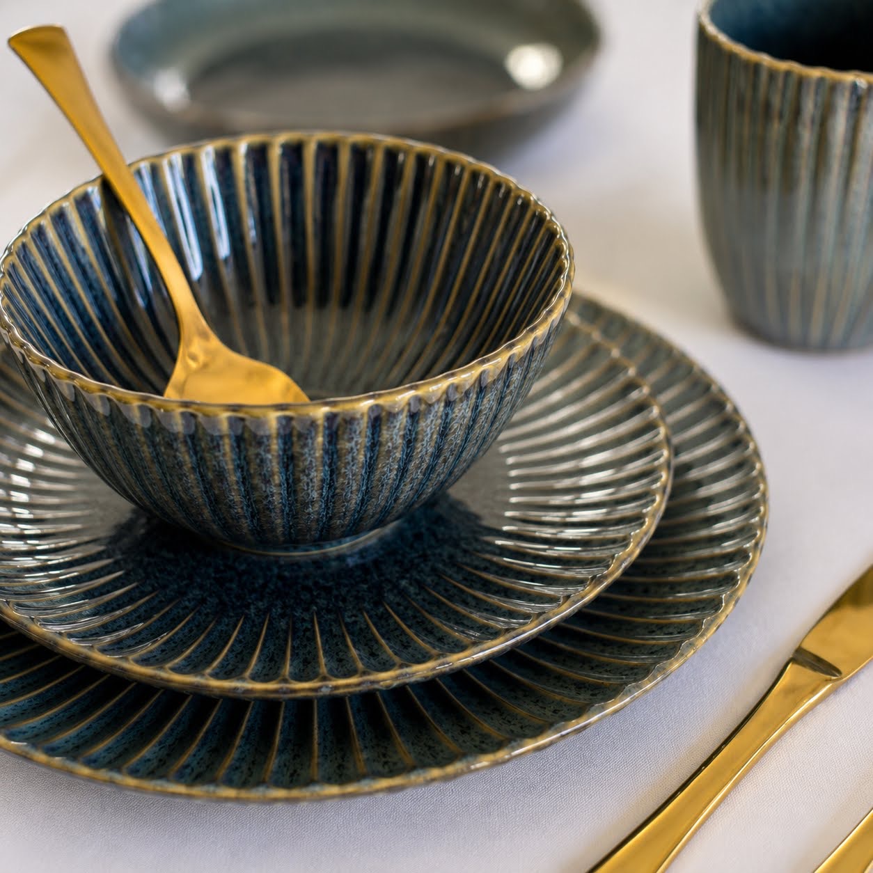 Conjunto de Louça de Mesa Azul Petróleo com Relevo Conjunto cerâmico azul com talheres dourados sobre mesa
