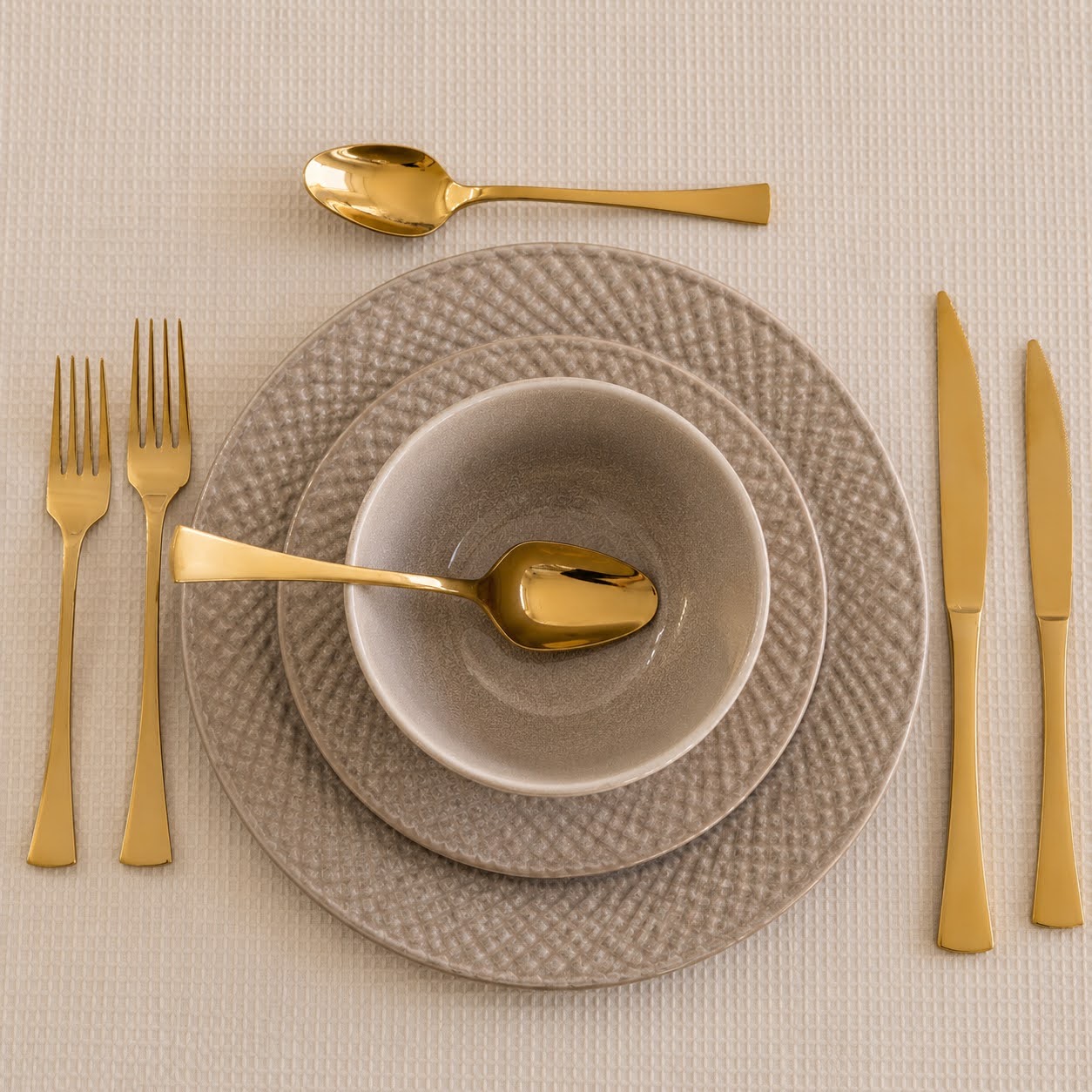 Conjunto de Louça de Mesa Bege Pérola em Grés Conjunto de talheres dourados e pratos cinzentos texturizados na mesa
