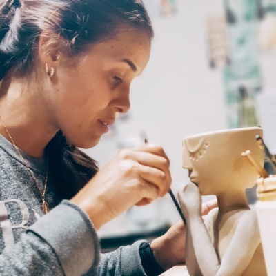 Mulher a pintar uma escultura de cerâmica bege em atelier