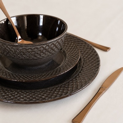 Conjunto cinza escuro texturado com tigela e talheres dourados numa mesa clara