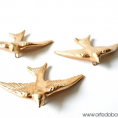 Três pêndulos de parede dourados em forma de pássaros sobre fundo branco