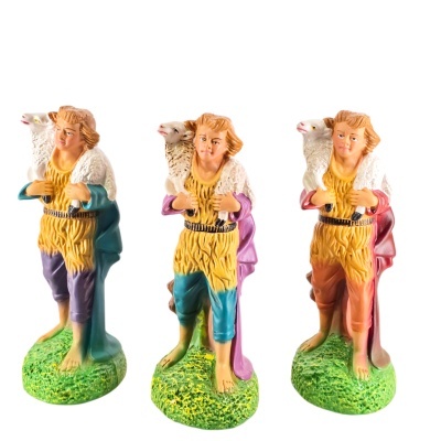 Três estátuas coloridas de homem com uma ovelha ao ombro sobre base verde