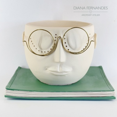 Vaso branco em forma de rosto com óculos dourados sobre livros