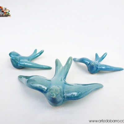 Três esculturas de pássaros em cerâmica azul brilhante sobre fundo branco