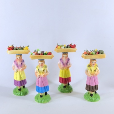 Quatro figuras femininas em miniatura com bandejas de frutas coloridas no topo