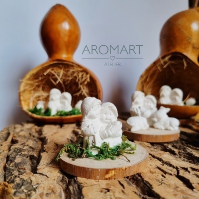 Figura decorativa de casal em resina sobre base de madeira com musgo, com bolas de madeira ao fundo numa superfície rústica.