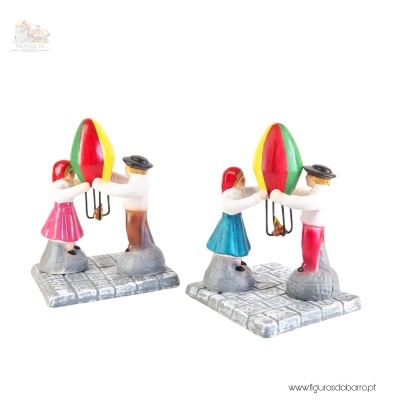 Figuras em cerâmica de um rapaz e uma rapariga segurando uma lanterna colorida sobre base que simula calçada.