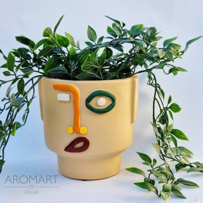 Vaso de cerâmica bege com rosto abstrato colorido e planta artificial verde