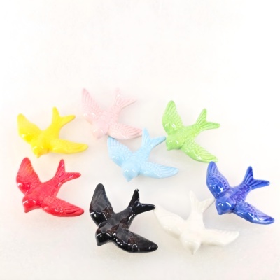 Sete pássaros cerâmicos coloridos dispostos em fundo branco.