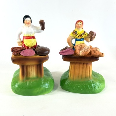 Figuras decorativas de mulheres a cortar carnes em trajes tradicionais sobre bases verdes