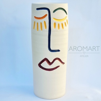 Vaso cerâmico branco com rosto pintado e texto AROMART ATELIER no fundo azul claro