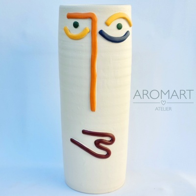 Vaso cerâmico branco com rosto abstrato em relevo colorido.