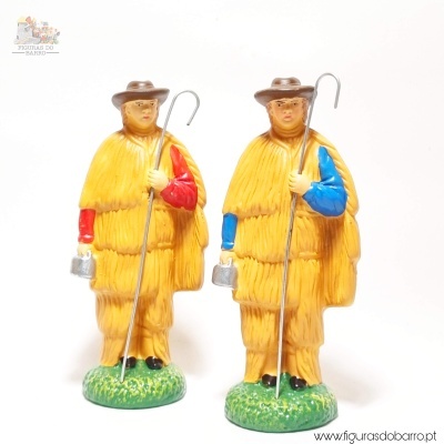Duas figuras decorativas de pastores com vestes amarelas, uma com manga vermelha e outra azul