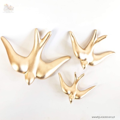 Três figuras decorativas douradas em forma de pássaros voando