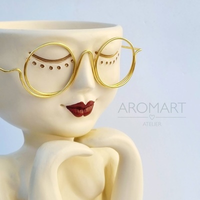 Escultura decorativa de rosto feminino com óculos dourados e detalhes pintados