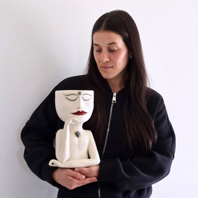 Estatueta de cerâmica branca com rosto decorado e mulher a segurar