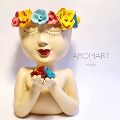 Vaso cerâmico em forma de rosto com flores coloridas e texto Aromart Atelier.