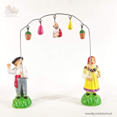 Figura decorativa de barro com homem e mulher em roupa tradicional e cinco objetos pendurados num arco metálico