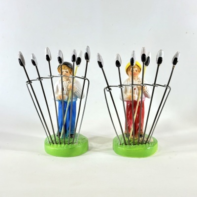 Dois suportes decorativos para pauzinhos com figuras humanas pintadas, bases verdes, 8 pauzinhos cada.