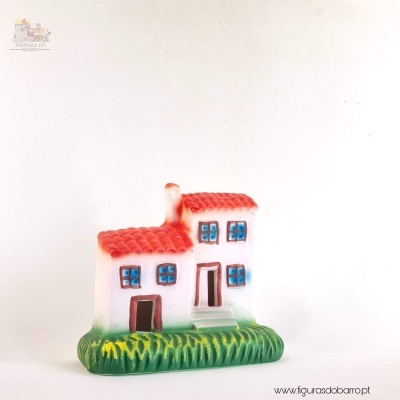 Miniatura cerâmica casa com telhado vermelho e janelas azuis sobre base verde