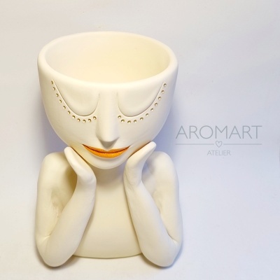Vaso decorativo branco em forma de rosto com lábios laranja e texto 'AROMART ATELIER' ao lado.