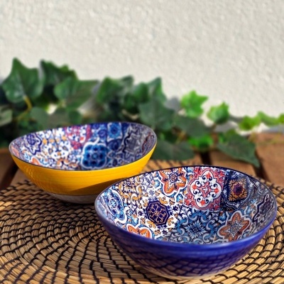 Duas taças coloridas em cerâmica sobre tapete de fibras naturais numa mesa de madeira