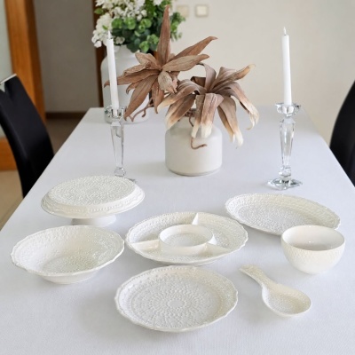 Conjunto branco de loiça com relevo floral em mesa branca com castiçais de vidro