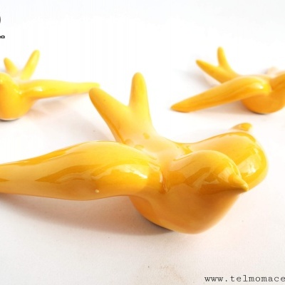 Três pássaros decorativos em cerâmica amarelos com acabamento brilhante sobre superfície branca