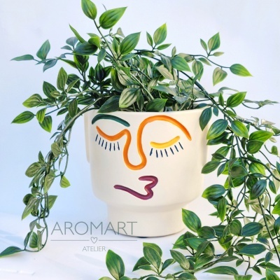 Vaso branco com rosto pintado e planta artificial de folhas verdes